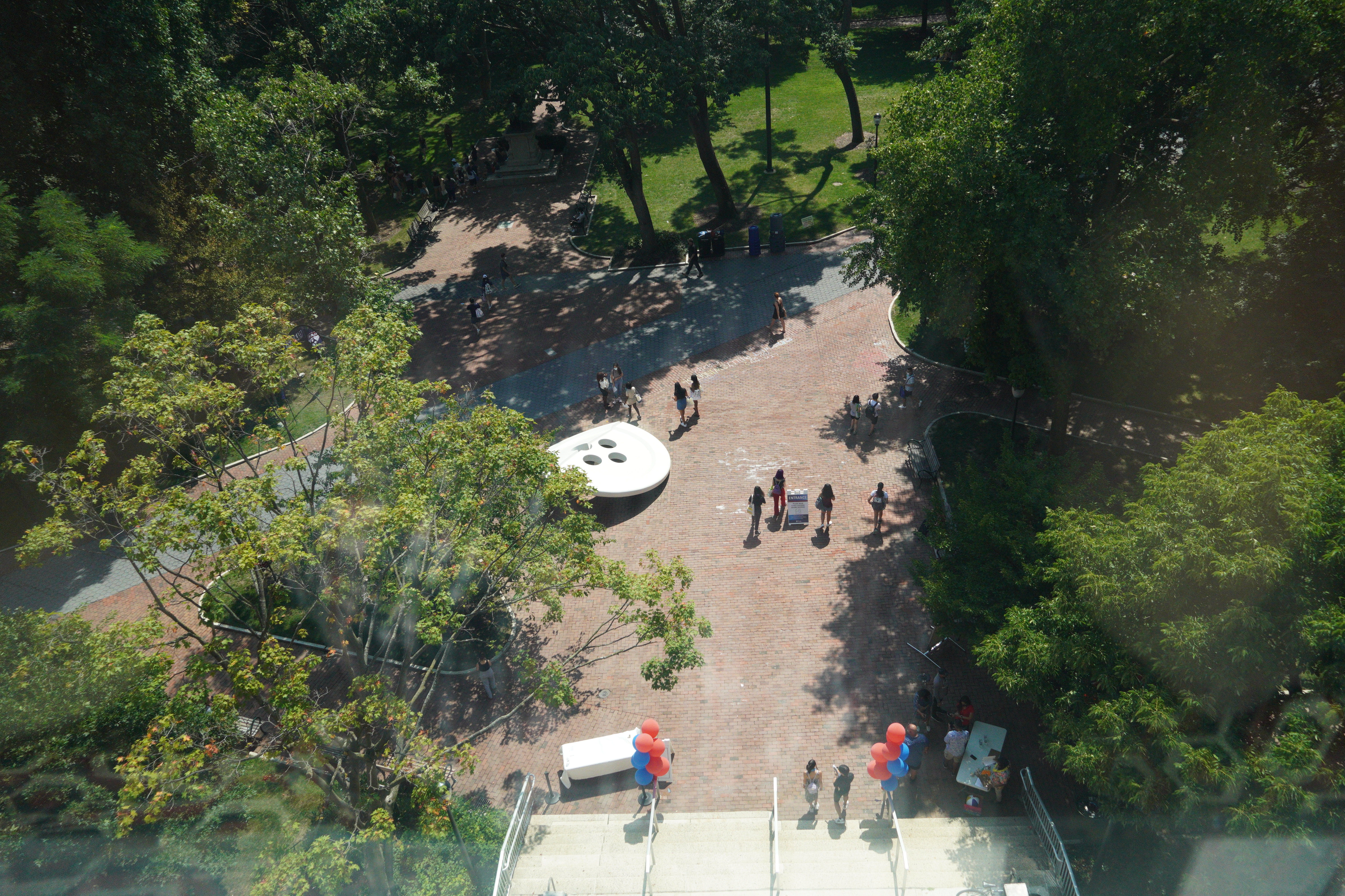 Looking down at the steps outside Van Pelt Library on a sunny day. There are red and blue balloons tied to the rails and about a dozen people are milling around.