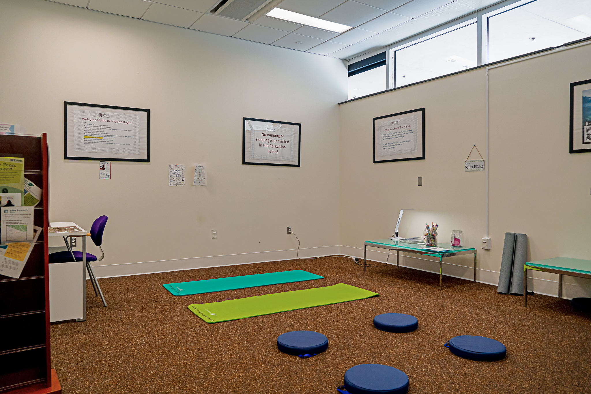 A room with a sign labeling it the Relaxation Room has two yoga mats and a variety of pillows on the floor.