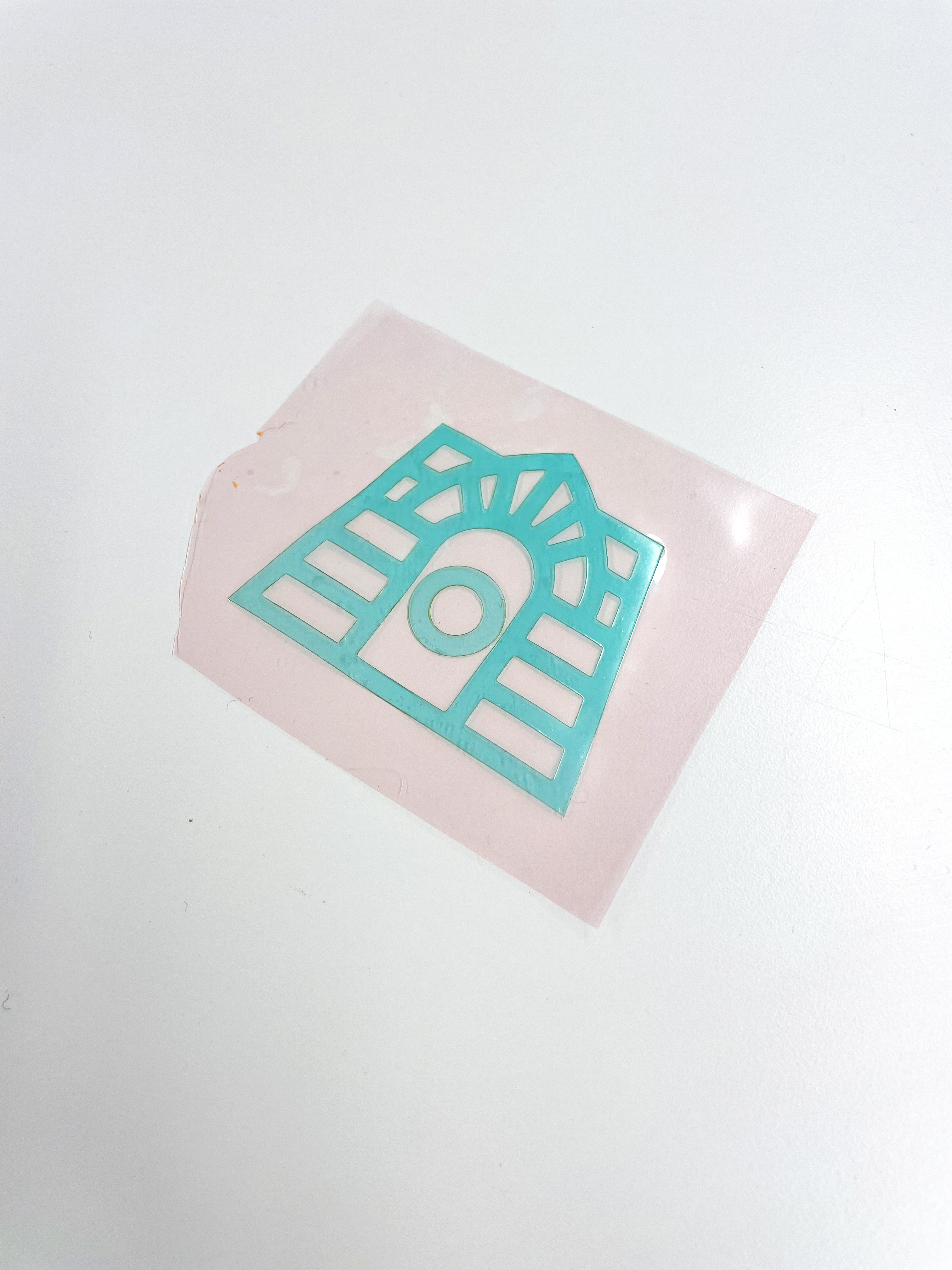  A translucent, pale pink square with a teal, geometric shape in the center, resembling a stylized archway, set against a white background.