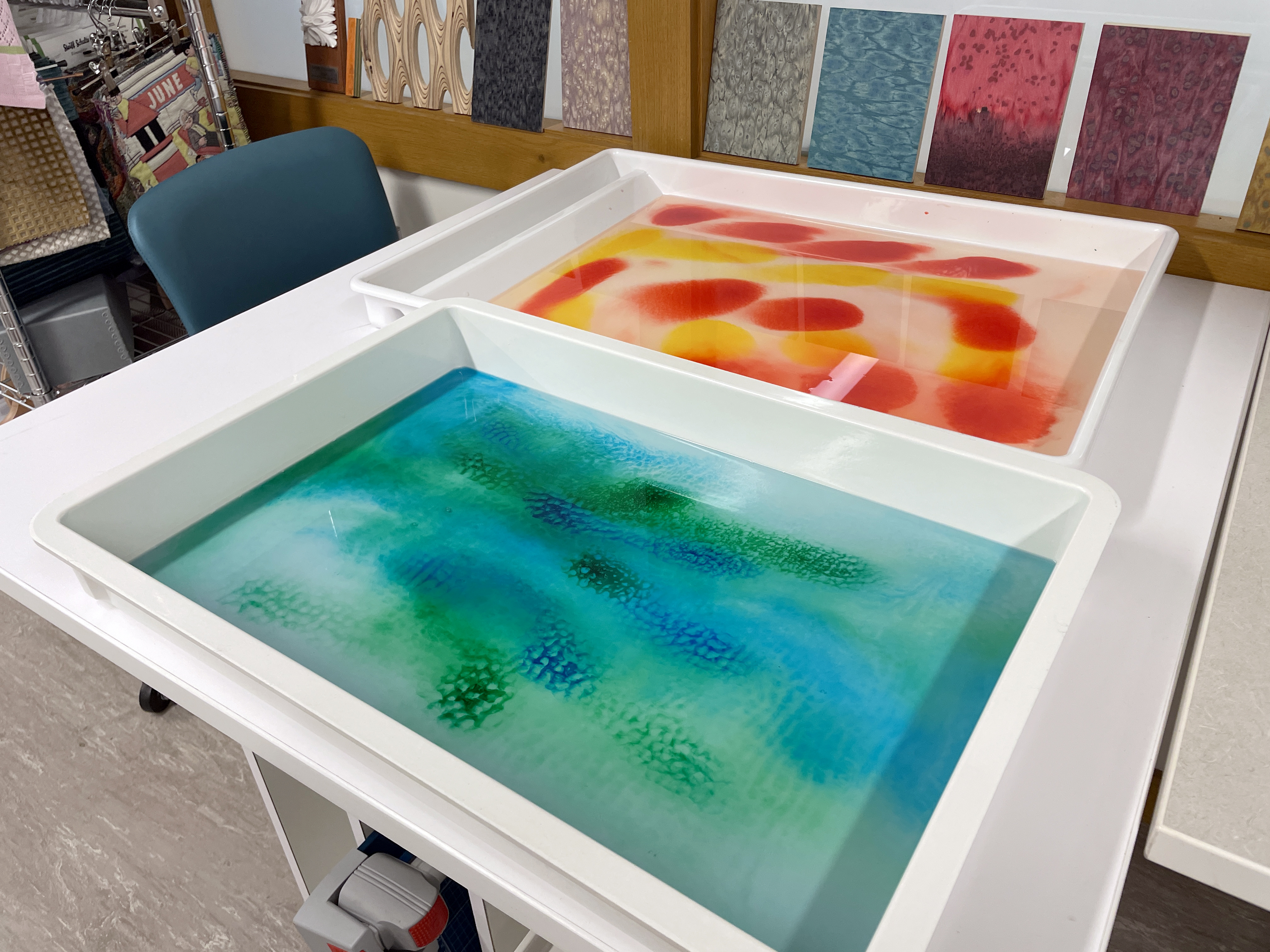 Two white trays on a table. The front tray holds a blue-green liquid, and the back tray contains yellow and red liquids.