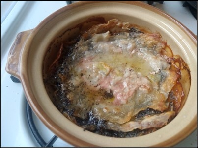A pastry-like flatbread in a glazed clay pot, covered in a mixture of rendered chicken juices and sugar syrup.